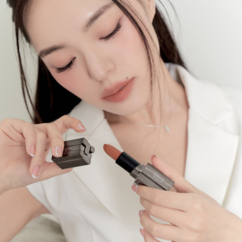 Matowa pomadka Muzigae Mansion Nuddy. Kobieta trzyma otwartą, metaliczną tubkę z aksamitnym wykończeniem.