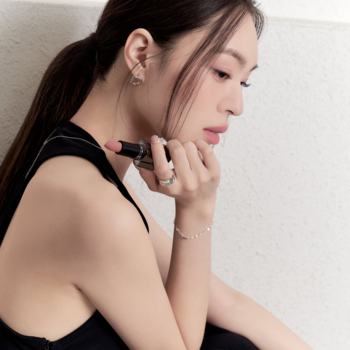 Kobieta trzyma matową pomadkę Muzigae Mansion Babe z wysuniętym nude sztyftem, ujęcie z profilu.