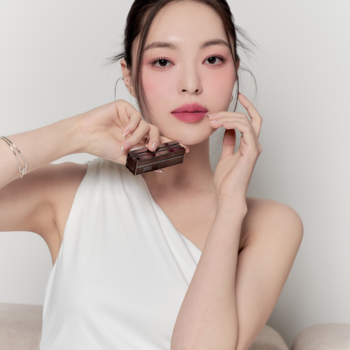 Kobieta trzyma w dłoni małą, ciemną matową pomadkę Muzigae Mansion Ruffle, prezentując odcień na ustach.