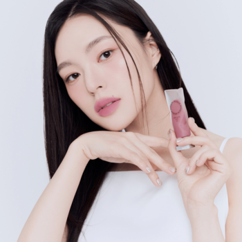 Kobieta z długimi włosami prezentuje matowy tint do ust Muzigae Mansion Posh, z efektem rozmycia na ustach.