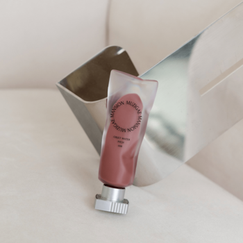 Matowy tint do ust Muzigae Mansion Pitch w różowej tubce, z efektem rozmycia, widok z przodu na jasnym tle.