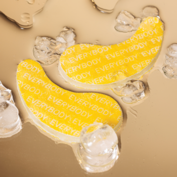 Dwa żółte hydrożelowe chłodzące płatki pod oczy EVERYBODY w kształcie banana, na beżowej cieczy z lodem.