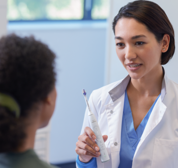 Dentystka prezentuje białą szczoteczkę Philips Sonicare z fioletową końcówką Sensitive pacjentce.