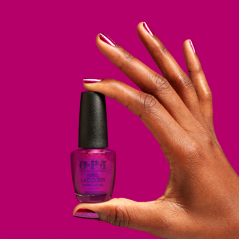 Ciemna dłoń trzyma mały lakier OPI Berry and Bright w odcieniu fuksji na różowym tle. Paznokcie pomalowane.