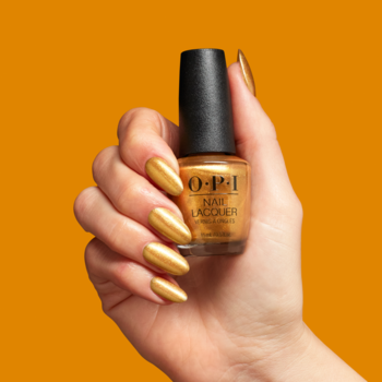 Dłoń z paznokciami pomalowanymi złotym lakierem OPI Nougat by Nature trzyma butelkę produktu na pomarańczowym tle.