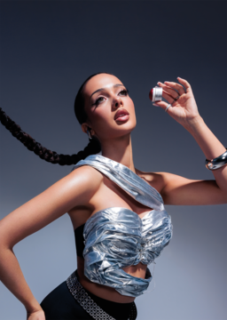 Kobieta w srebrnym topie trzyma otwarty Cream Blush Cosmic Flush, czerwony kremowy róż w sticku, na szarym tle.