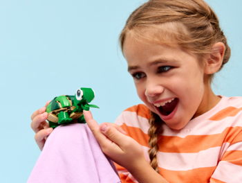 Szczęśliwa dziewczynka z warkoczami podziwia zielonego żółwia LEGO Creator 3 w 1, trzymanego w dłoniach.