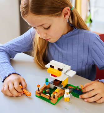 LEGO Minecraft Farma kurczaków 21585: dziewczynka buduje biały kurnik-kurczak z figurkami i akcesoriami, widok z góry.