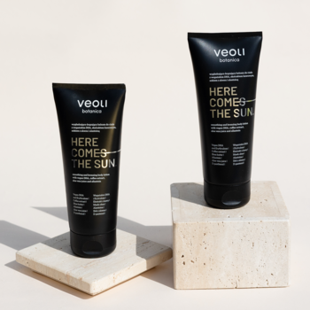Dwa czarne balsamy Veoli Botanica Here Comes The Sun, wygładzająco-brązujące, w dwóch rozmiarach, na beżowych podstawkach.