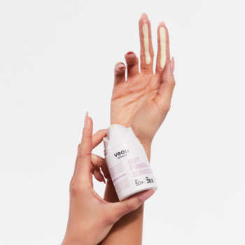 Dłoń trzyma Veoli Botanica But First Sunscreen SPF 50+, biała butelka, test kremu na skórze, białe tło.