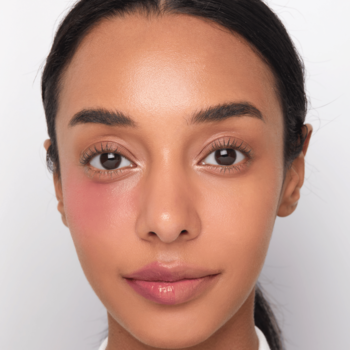 Zbliżenie na kobietę z różowym balsamem Kaja Dewy Bar Berry Sparkler na lewym policzku i ustach, efekt glow.