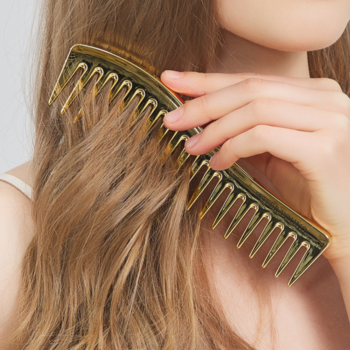 Dłoń czesząca falowane włosy złotym, antystatycznym grzebieniem ZURI Sister Young z szerokimi zębami.