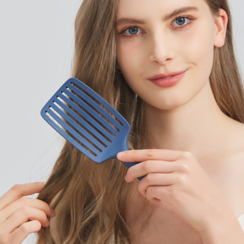 Kobieta czesze długie, falowane włosy niebieską, wentylowaną szczotką Ovia Sister Young z włosiem dzika.