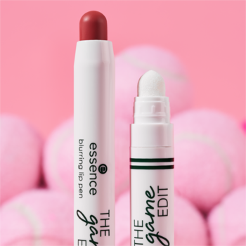 Essence blurring lip pen i aplikator The Game Edit, białe, z czerwoną końcówką, na tle różowych piłek tenisowych.
