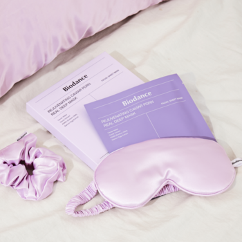 Biodance Bio-Collagen Real Deep Mask PDRN i kawior, lawendowe opakowania, jedwabna opaska i scrunchie na łóżku.