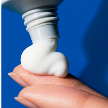 Zbliżenie: biały krem do twarzy Uriage wyduszany z tubki na palec, niebieskie tło. Ulga dla suchej skóry.