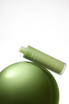 Zielona butelka toniku TIRTIR Protective Skin Toner (150ml) leży na boku na odblaskowej kuli, z kroplą opadającą z otworu.