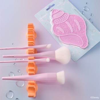 Różowy zestaw pędzli do makijażu w pomarańczowych uchwytach suszących oraz silikonowa myjka w kształcie muszli.