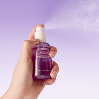Dłoń rozpyla fioletową butelkę Biodance Caviar PDRN Serum Mist, z której unosi się lekka żelowa mgiełka.