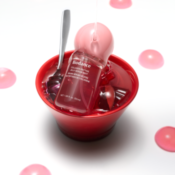Biodance Collagen Peptide Jelly Serum Mist w czerwonej butelce w misce z galaretką, z łyżką i różowymi kroplami na białym tle.