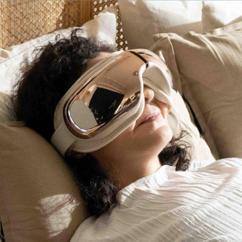 Inteligentny masażer oczu RENPHO Eyeris 3 Rose Gold na oczach zrelaksowanej kobiety leżącej w łóżku.