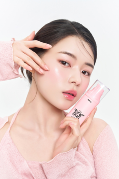 Modelka z promienną, różaną cerą prezentuje EDIT.B Sunday Pink Tone-Up Sun Serum SPF 50+ w przezroczystej butelce z pompką.