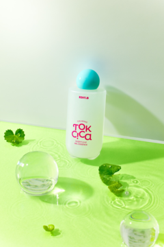 EDIT.B Calming Tok Cica Heartleaf Gel Essence, matowa butelka z turkusową nakrętką na zielonym, wodnistym tle z liśćmi.