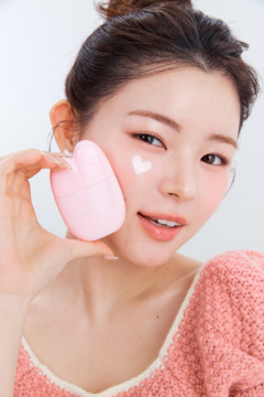 Rozświetlający krem SPF 50 EDIT.B Bare Bunny 01 Pink w sercowatym opakowaniu, kobieta z kremem na policzku.