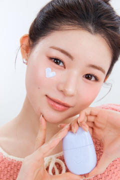 Kobieta trzyma korekcyjny krem SPF 50 EDIT.B Bare Bunny 02 Purple, z fioletowym sercem na policzku.