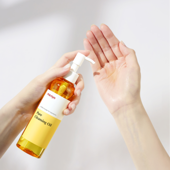Żółty ma:nyo Pure Cleansing Oil w przezroczystej butelce z pompką, dłoń dozuje olejek oczyszczający do usuwania zaskórników.