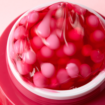 TXA Niacinamide Capsule Cream, rozjaśniający krem. Zbliżenie na czerwony żel z różowymi kapsułkami w słoiczku pod folią.
