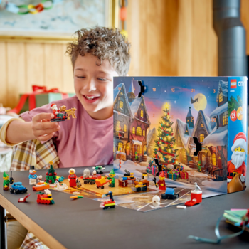 Uśmiechnięty chłopiec bawi się LEGO City Kalendarzem adwentowym 60510. Wokół rozłożone świąteczne minifigurki i modele.
