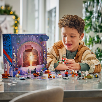 Uśmiechnięty chłopiec bawi się otwartym Kalendarzem adwentowym LEGO Star Wars 75456 i jego świątecznymi figurkami.