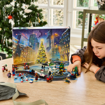 Dziewczynka bawi się LEGO Marvel Kalendarz Adwentowy 76340. Na drewnianym stole minifigurki i świąteczne akcesoria z zestawu.