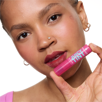 Zaczerwieniona twarz i usta kobiety, która trzyma różowy pisak essence JUICY TINT 05 Plum Party o śliwkowym zapachu.