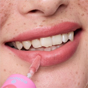 Zbliżenie na usta z piegami, z aplikatorem różowego tintu essence JUICY TINT 04 Raspberry Rush. Widać malinowy kolor na wargach.