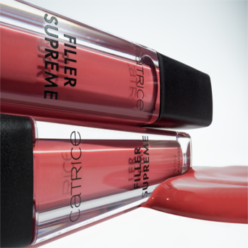 Dwa błyszczyki Catrice Filler Supreme Lip Gloss, jagodowy odcień. Zboczne ujęcie na przezroczyste tubki, z wylanym błyszczykiem.