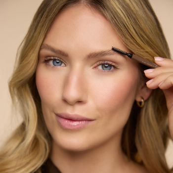 Kobieta modeluje brwi kredką Ultra Fine Brow Liner z wbudowaną szczoteczką, precyzyjnie definiując ich kształt.