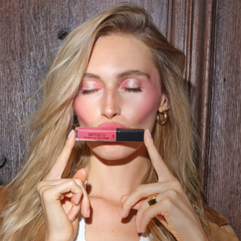 Blondynka z różowym makijażem trzyma Artdeco Hydra Lip Booster Translucent Mountain Rose, błyszczyk nawilżający.
