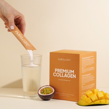 Ręka wsypuje Premium Collagen Natu.Care mango-marakuja z saszetki do szklanki obok owoców i opakowania.