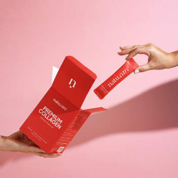 Ręce na różowym tle: jedna trzyma otwarte opakowanie, druga wyciąga czerwoną saszetkę Natu.Care Premium Collagen.