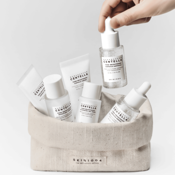 Zestaw SKIN1004 Tone Brightening Travel Kit do rozjaśniania przebarwień, ręka aplikuje serum z kroplomierzem.