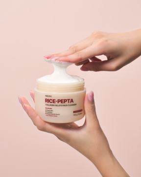 Dłonie wyciskające biały żel-maskę Nacific Rice Pepta Collagen Gelato Pack Cleanser z beżowego słoika na różowym tle.