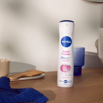Biały dezodorant NIVEA Fresh Flower bez aluminium, z różowym kwiatem na etykiecie, stoi na drewnianym blacie.