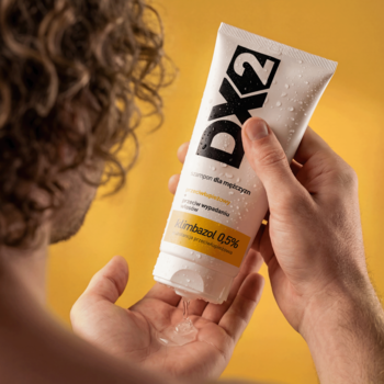 Mężczyzna wyciska DX2 szampon przeciwłupieżowy z mokrej białej tubki na dłoń. Widoczne logo i klimbazol 0,5%.