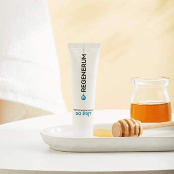 Biała tuba Regenerum regeneracyjne serum do pięt z 30% mocznikiem, pionowo na tacy z miodem.