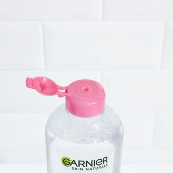 Zbliżenie na Płyn Micelarny Garnier Skin Naturals 3w1 z bąbelkami, otwartą różową nakrętką na białych kafelkach.
