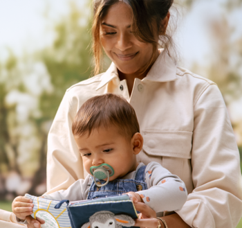 Zielony smoczek ortodontyczny 6-18m+ z dużymi otworami powietrznymi w ustach dziecka trzymanego przez matkę.