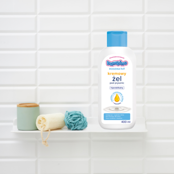 Bambino Rodzina kremowy żel pod prysznic 400 ml na białej półce z gąbkami, biała butelka, niebieska nakrętka.