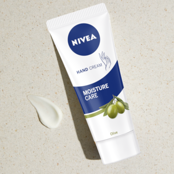 NIVEA Moisture Care krem do rąk z oliwą z oliwek, biała tubka z zielonymi liśćmi, widok pod kątem na beżu.